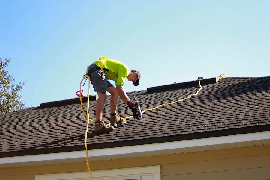 Roofing professional working across a slope of asphalt shingles in bright sunlight
