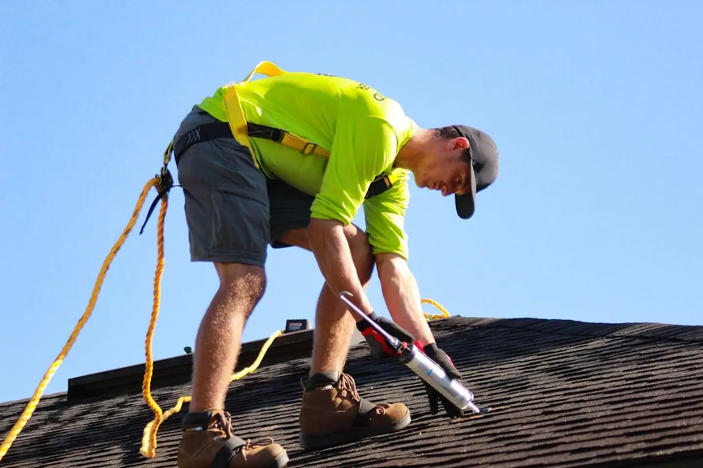 Roofer harnessed on an asphalt shingle roof, sealing a flashing detail by hand