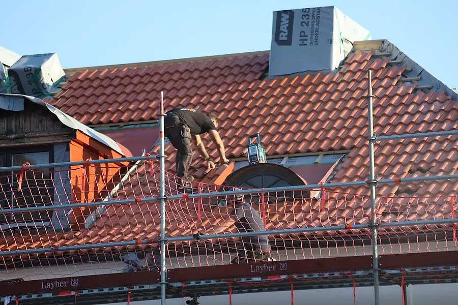 Roofers working on a terracotta tile roof from scaffolding